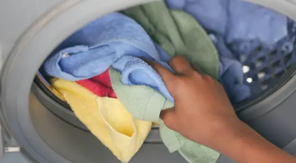 Hand pakt kleurrijke handdoeken en ondergoed uit de wasmachine.