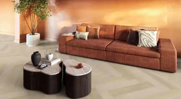 Een woonkamer met een oranje bank, marmeren tafels en een plant. De lichte evc vloer met visgraatmotief vormt een rustige basis.