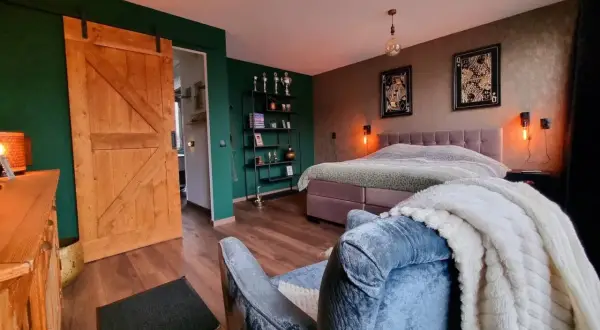 Slaapkamer met groene muur, houten schuifdeur en een bed met een deken met een subtiel ombre effect.