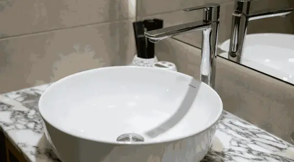 Moderne witte wasbak met een glanzende kraan. Er zijn lichte krassen in de wasbak te zien, die het dagelijks gebruik verraden.