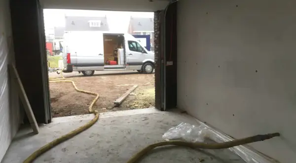 Grote gele slang voor zand stralen in een garage, met een busje buiten.