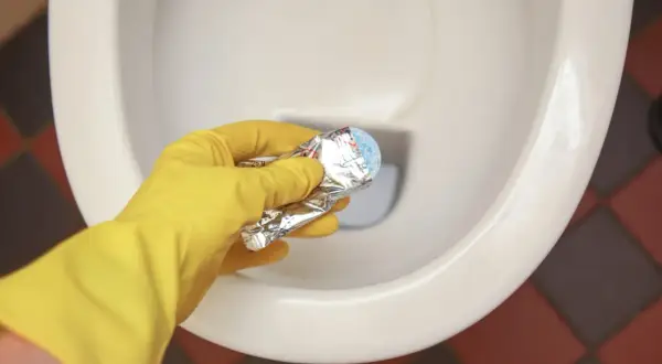 Gele handschoen houdt product vast om kalkrand wc pot te verwijderen.