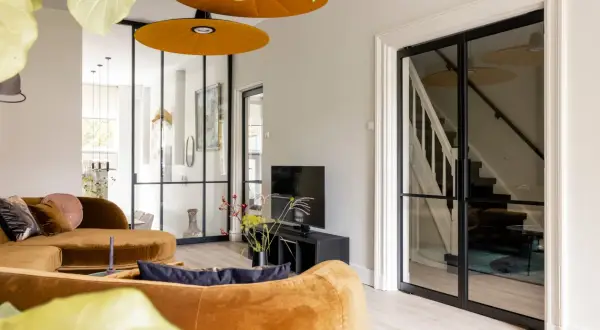 Gezellige woonkamer met oranje bank, glazen deuren naar de trap en een ontspullen lijst.