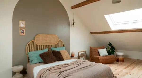 Gezellige slaapkamer verbouwen met rieten hoofdbord, zachte plaids en een comfortabele fauteuil onder het dakraam.