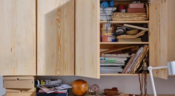 Een open houten kast met diverse spullen, waaronder stapels oud papier, tijdschriften en bakjes. Ideaal voor oud papier opbergen.