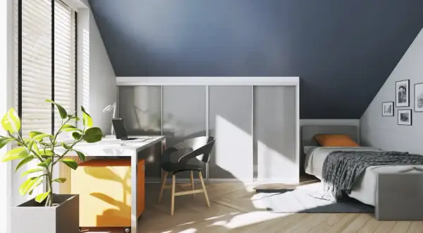 Een smalle hal met een bureau, bed en kasten. De zon schijnt door het raam en werpt patronen op de houten vloer.