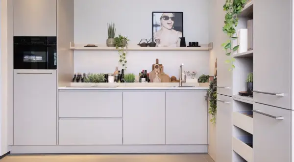 Moderne nis keuken met ingebouwde oven, strakke kasten en decoratieve planten. Een poster met een lachende vrouw siert de muur.