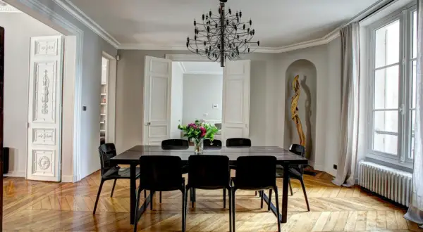 Elegant Frans interieur met een grote eettafel, zwarte stoelen, een opvallende kroonluchter en een houten vloer.