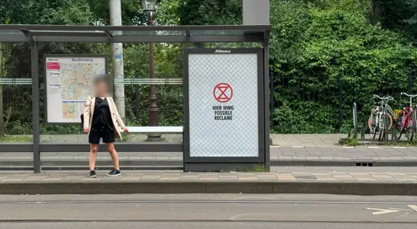 Een poster bij een bushalte met een symbool en de tekst "HIER HING FOSSIELE RECLAME". Dit is een oproep om geadresseerde reclame stopzetten.