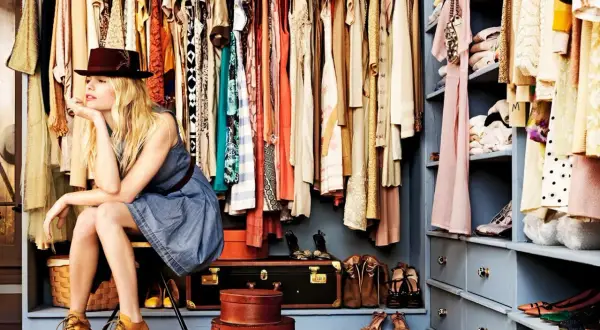 Vrouw met hoed in een volle kast, kleding opruimen moeilijk. Veel kleding en schoenen, een uitdaging om te organiseren.