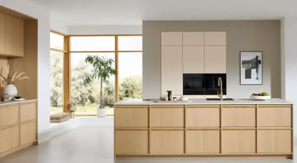 Een lichte, minimalistische keuken met houten kasten, een groot raam en een groene plant.