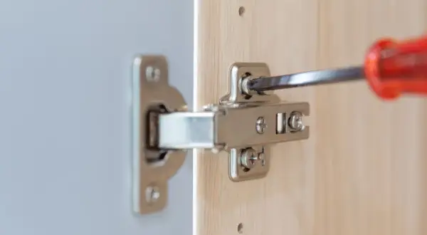 Met een schroevendraaier worden twee schroeven van een scharnier bijgesteld om de kastdeur perfect te laten sluiten.