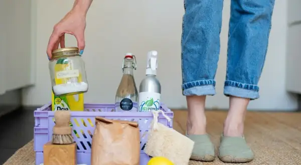 Een mand met spullen voor duurzaam schoonmaken: citroenzuur, azijn, zeep, borstel, citroen en een loofah.