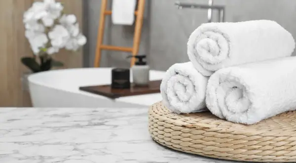 Frisse, witte handdoeken, net gewassen, liggen op een mandje in een luxe badkamer.