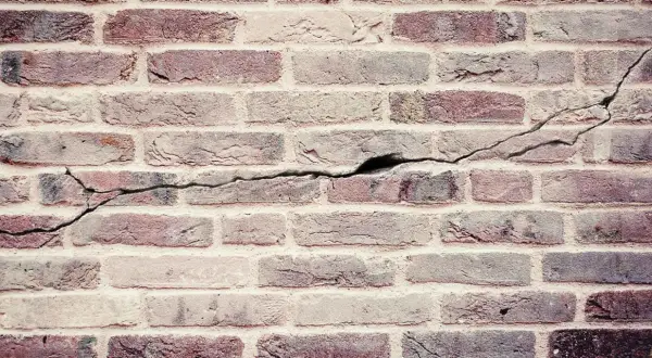 Een oude bakstenen muur met duidelijke scheuren die door de stenen lopen, getuigen van de tand des tijds.