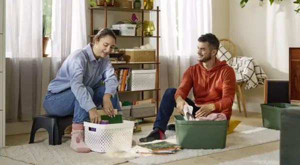 Een stel pakt spullen in, klaar voor hun reis van ontspullen in 52 weken. Ze sorteren boeken en kleding in opbergbakken.