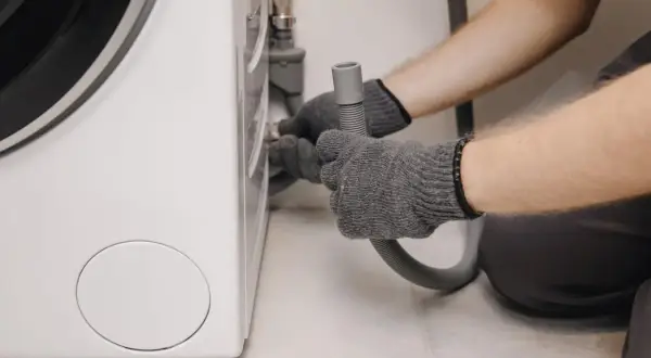 Grijze handschoenen bevestigen een slang aan een wasmachine, mogelijk om wasmachine problemen op te lossen.
