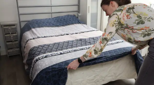 Vrouw verschoont bed met een bloemenblouse. Een schone slaapomgeving is belangrijk, dus vraag je je af hoe vaak bed verschonen?