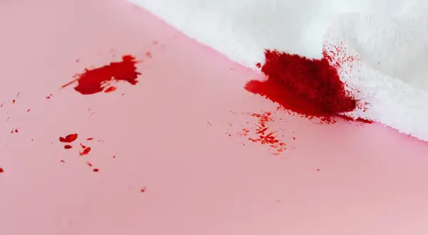 Bloedvlekken verwijderen? Oma weet raadt! Een witte doek absorbeert rode vlekken op roze ondergrond.