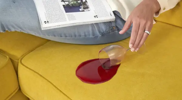 Een glas rode wijn is omgevallen op een gele bank. Hopelijk ruikt de bank straks weer lekker fris!