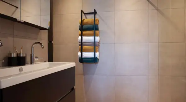 Netjes opgestapelde handdoeken in verschillende kleuren op een zwarte handdoekenrek in een moderne badkamer.