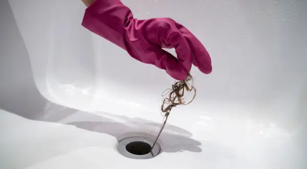 Roze handschoen verwijdert haar uit doucheputje om verstoppingen te voorkomen.