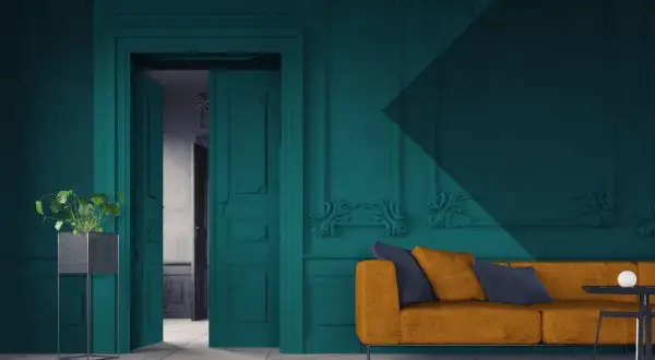 Een modern interieur waar groen en blauw combineren. Een okergele bank met donkerblauwe kussens staat voor een diepblauwe muur met sierlijke ornamenten.