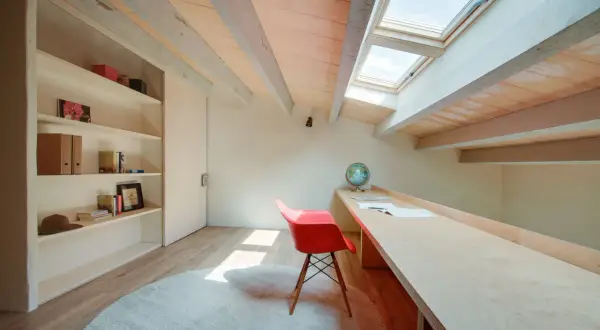 Een opgeruimde zolder met een bureau, boekenkast en dakramen. Perfect voor een rustige werkplek.