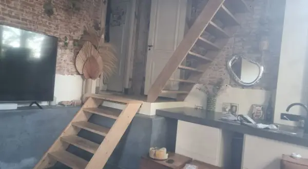 Een vide met een houten trap, bakstenen muur en een tv. Wat is een vide? Een open ruimte in een huis die meerdere verdiepingen verbindt.