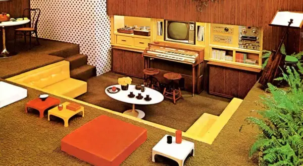 Een retro woonkamer met een **zitkuil jaren 70**, oranje en gele meubels, een orgel en een tv.