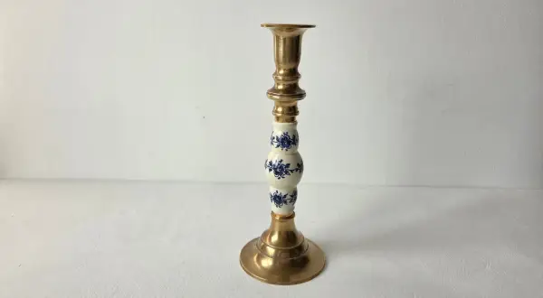 Een gouden kandelaar met een wit porseleinen deel, versierd met blauwe bloemen. Dit is wat vintage is: een stukje geschiedenis dat warmte en sfeer brengt.