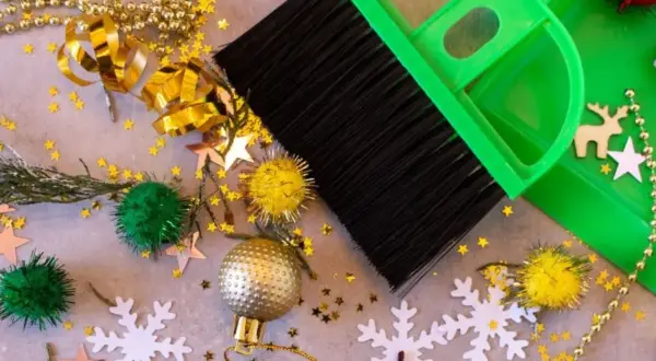 Een groene bezem en stoffer maken de kerstspullen op, met glitters, kerstballen en sneeuwvlokken verspreid.