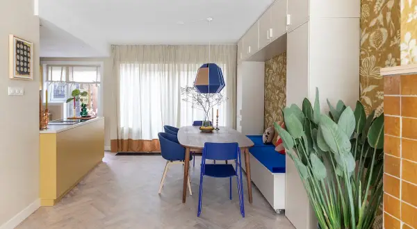 Een moderne eetkamer met een gele keuken en blauwe stoelen. De RAL 7006 combineren met de blauwe en gele accenten zorgt voor een levendige sfeer.