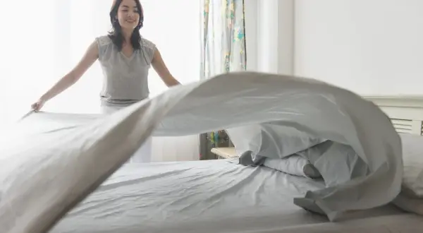 Vrouw verschoont beddengoed, zodat de slaapkamer lekker laat ruiken.