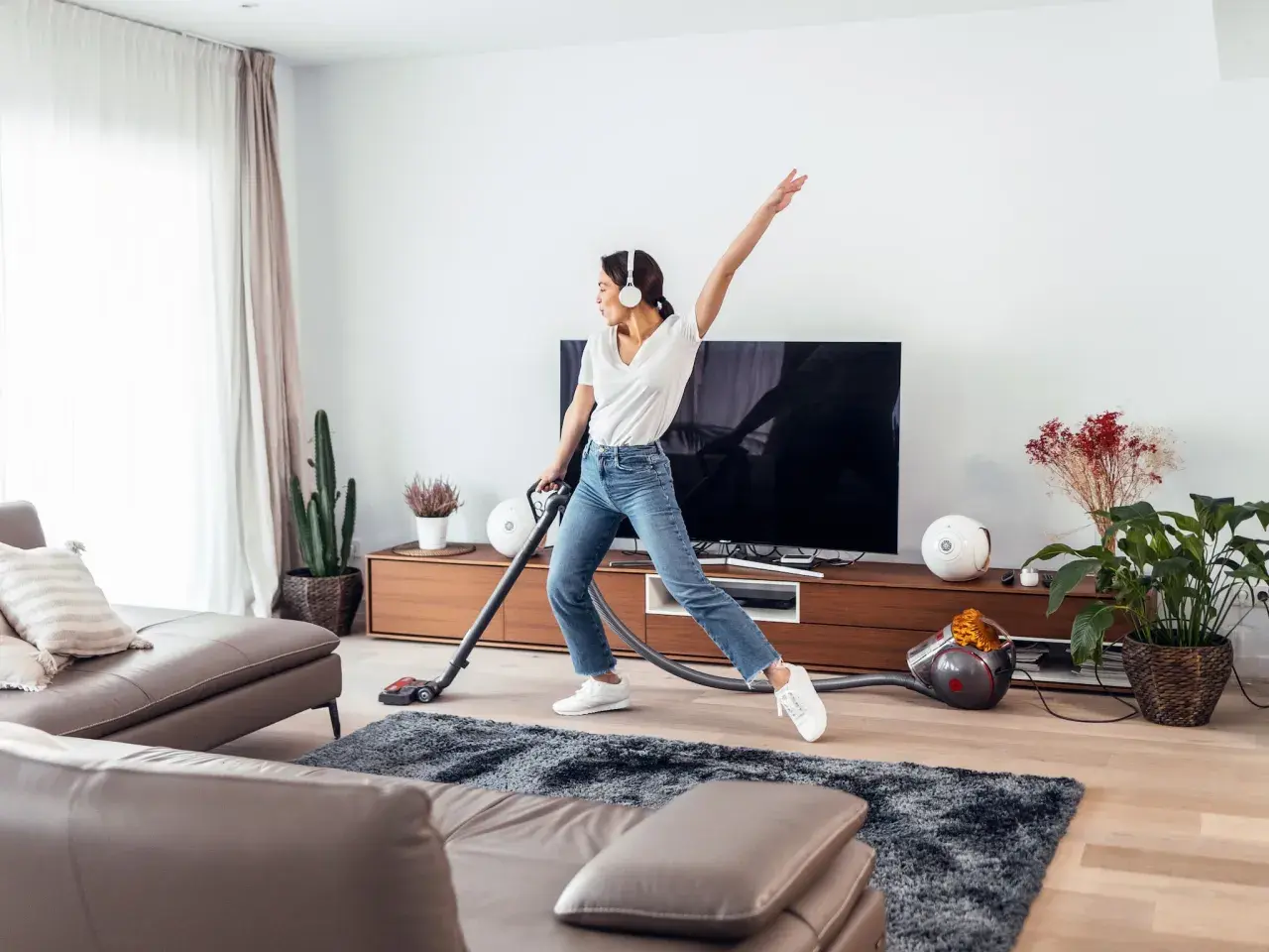 Vrolijke vrouw met koptelefoon danst tijdens de voorjaarsschoonmaak met de stofzuiger.