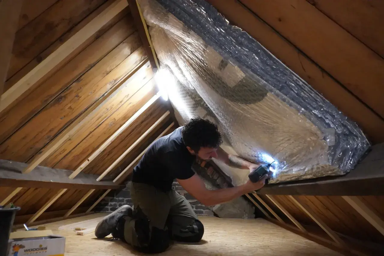 Man isoleert de zolder met reflecterend materiaal. Zo wordt de warmte in huis gehouden en bespaart hij op energiekosten.