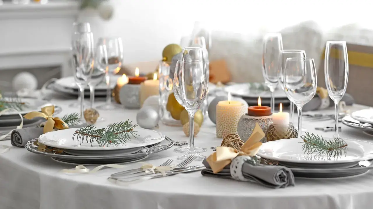 Een feestelijk gedekte tafel met glazen, kaarsen, kerstballen en dennentakjes. Klaar voor een gezellig diner!