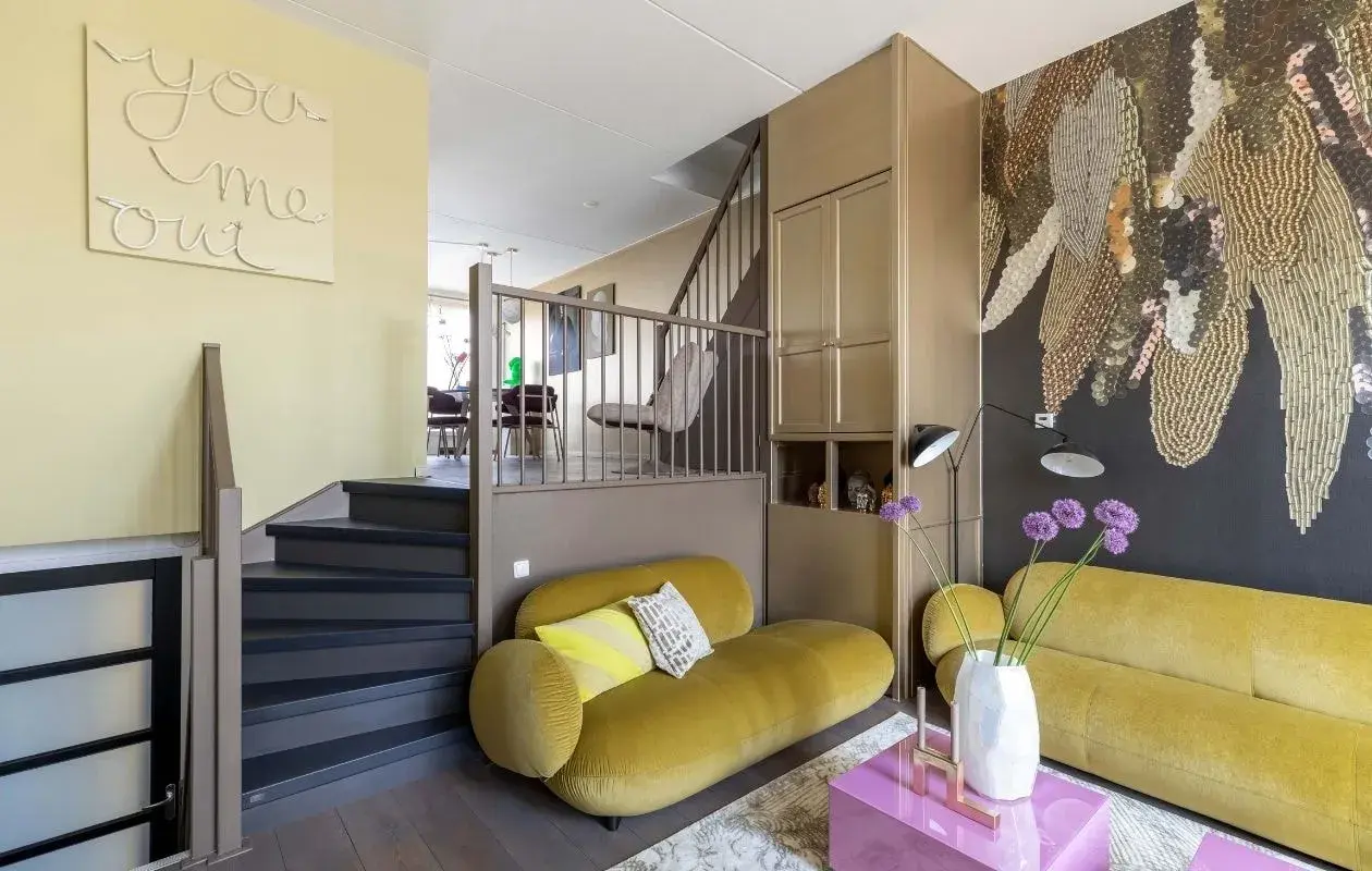 Gezellige split level woning met gele bank, trap en opvallende muurdecoratie.