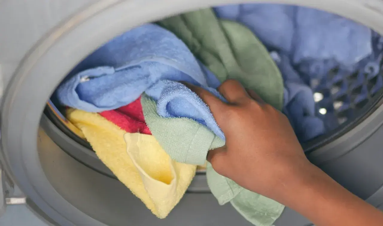 Hand pakt kleurrijke handdoeken en ondergoed uit de wasmachine.