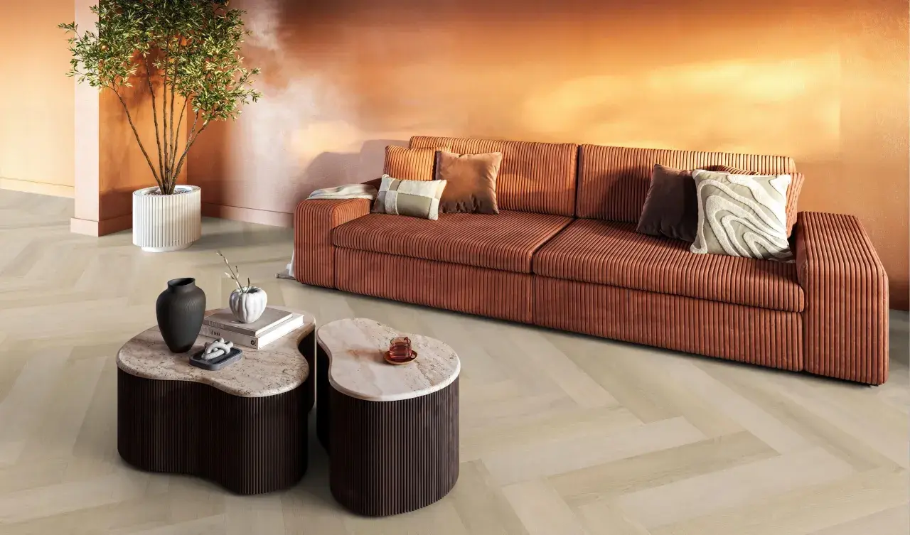 Een woonkamer met een oranje bank, marmeren tafels en een plant. De lichte evc vloer met visgraatmotief vormt een rustige basis.