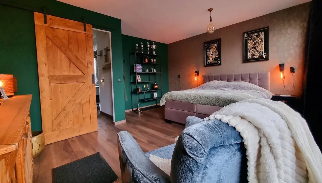 Slaapkamer met groene muur, houten schuifdeur en een bed met een deken met een subtiel ombre effect.