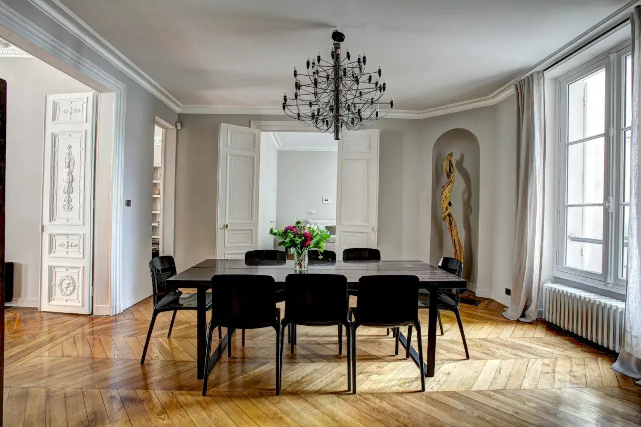 Elegant Frans interieur met een grote eettafel, zwarte stoelen, een opvallende kroonluchter en een houten vloer.