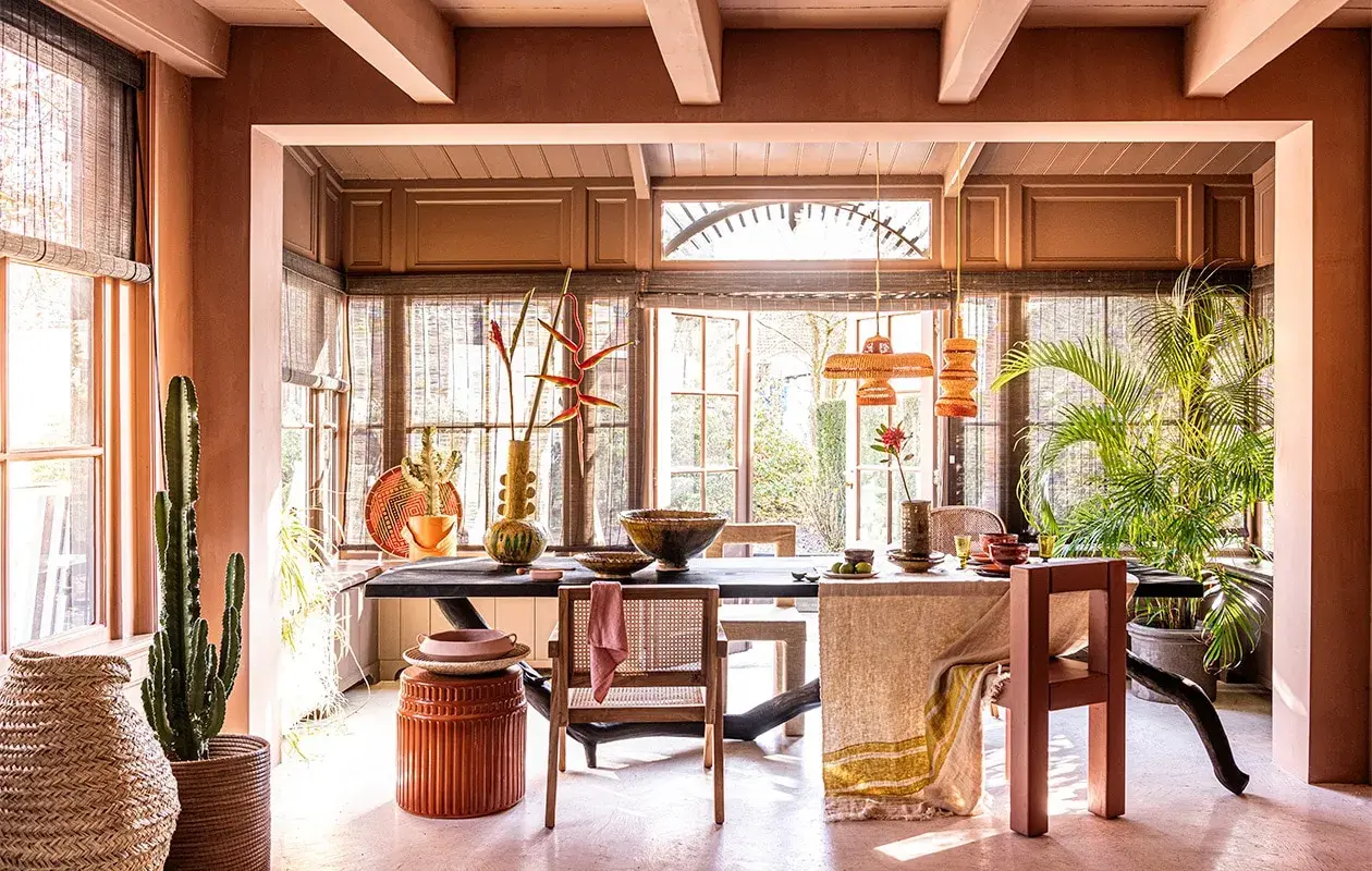 Warme, aardse tinten domineren deze eetkamer. De balken van het plafond zijn geschilderd in een lichte kleur, wat een mooi contrast vormt met de terracotta muren.