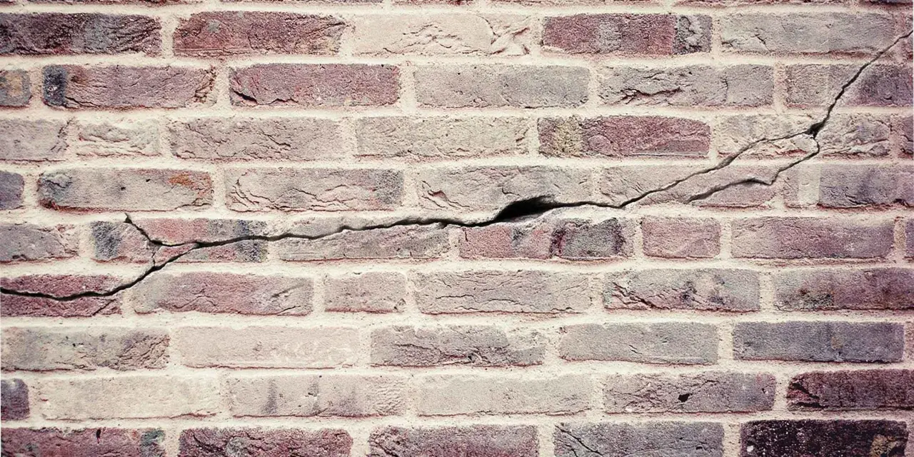 Een oude bakstenen muur met duidelijke scheuren die door de stenen lopen, getuigen van de tand des tijds.