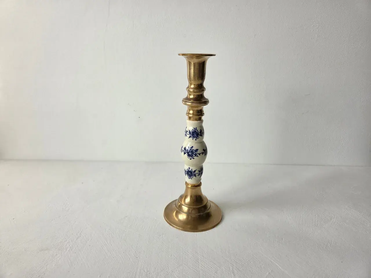 Een gouden kandelaar met een wit porseleinen deel, versierd met blauwe bloemen. Dit is wat vintage is: een stukje geschiedenis dat warmte en sfeer brengt.