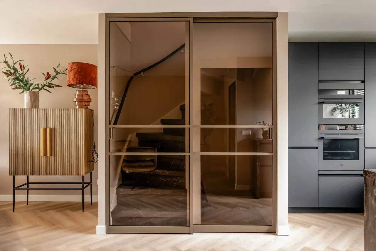 Moderne glazen schuifdeuren geven trapgat inspiratie. Een marmeren trap met donkere treden en een houten vloer.