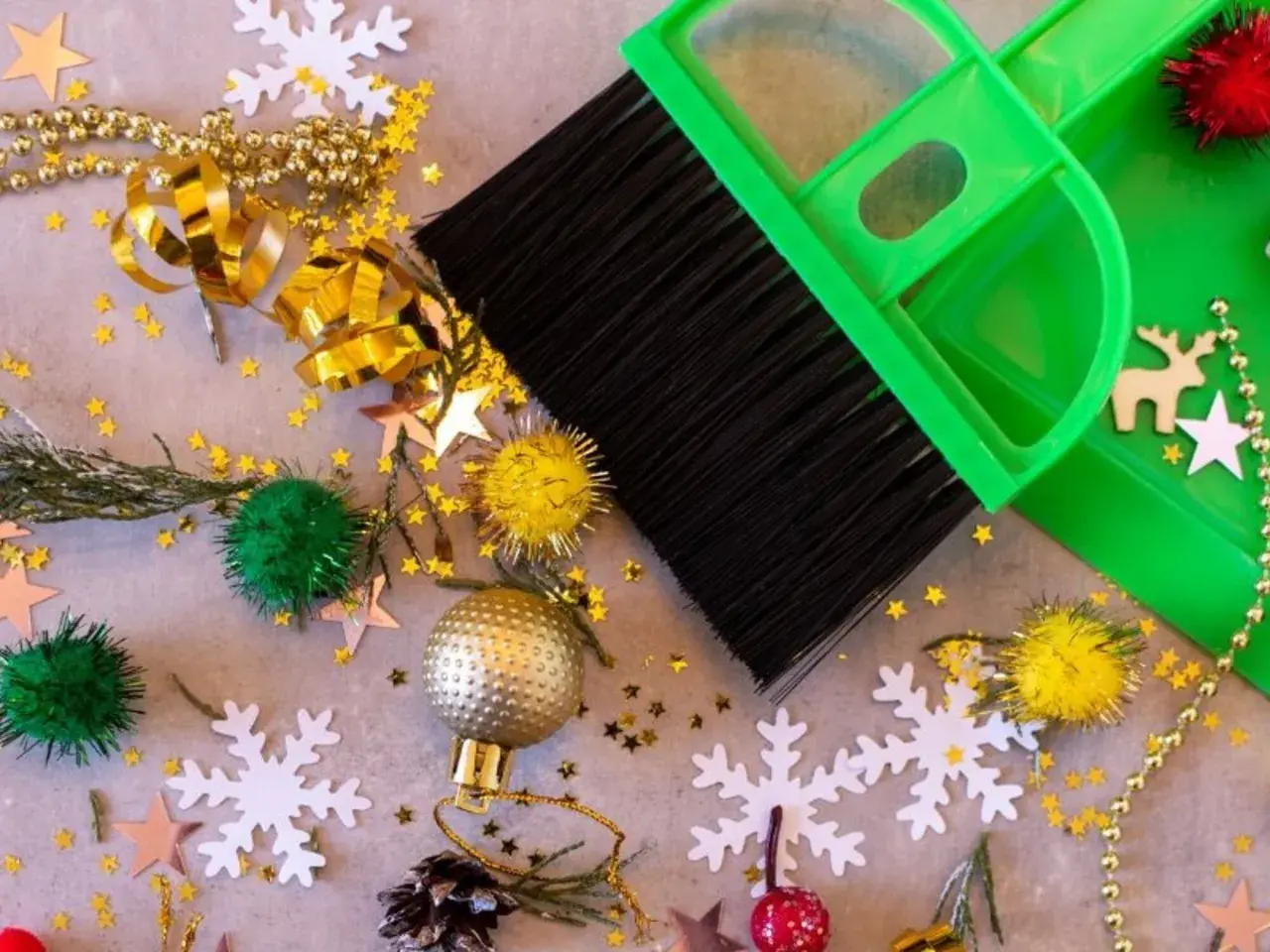 Een groene bezem en stoffer maken de kerstspullen op, met glitters, kerstballen en sneeuwvlokken verspreid.