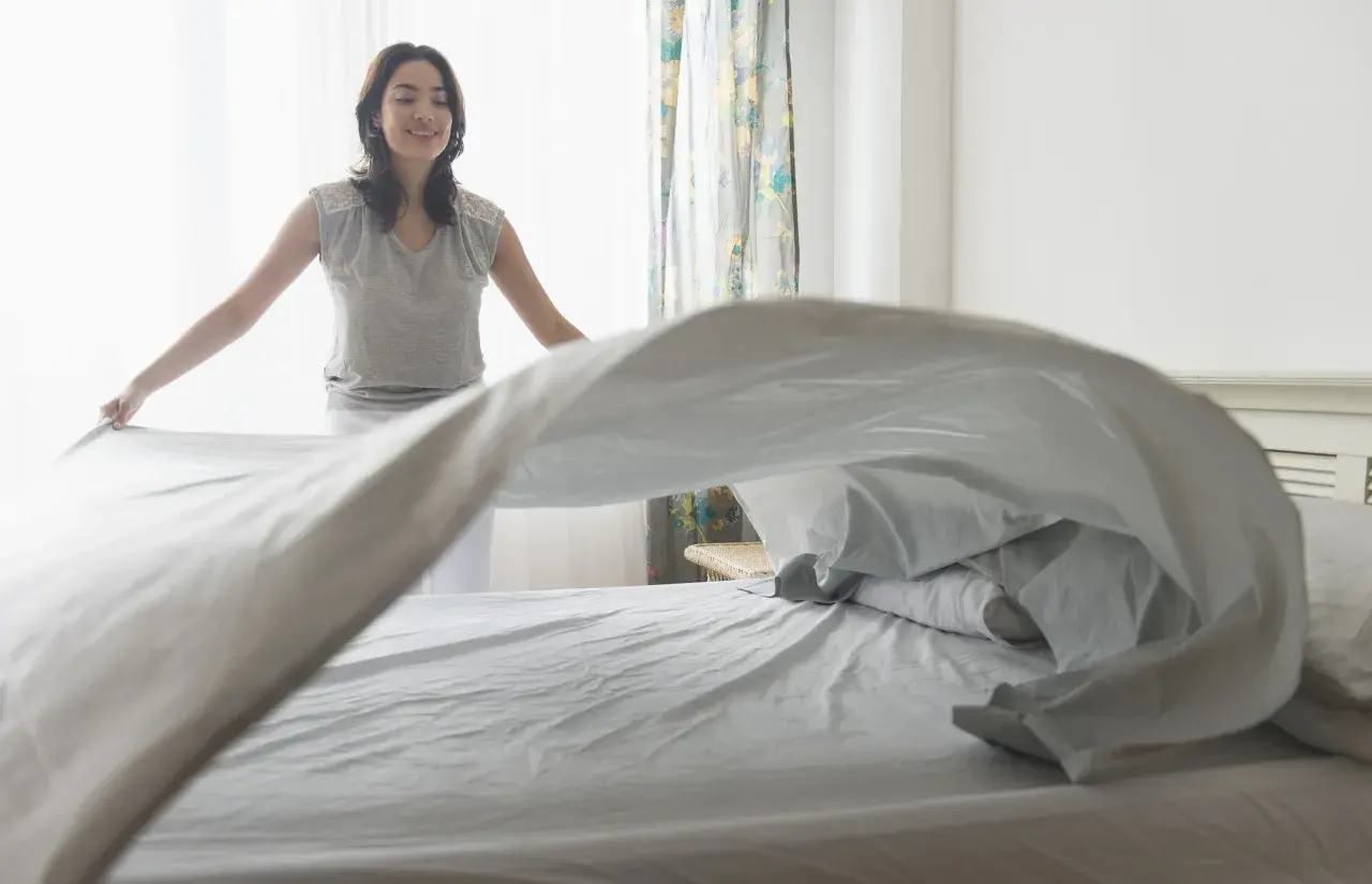 Vrouw verschoont beddengoed, zodat de slaapkamer lekker laat ruiken.