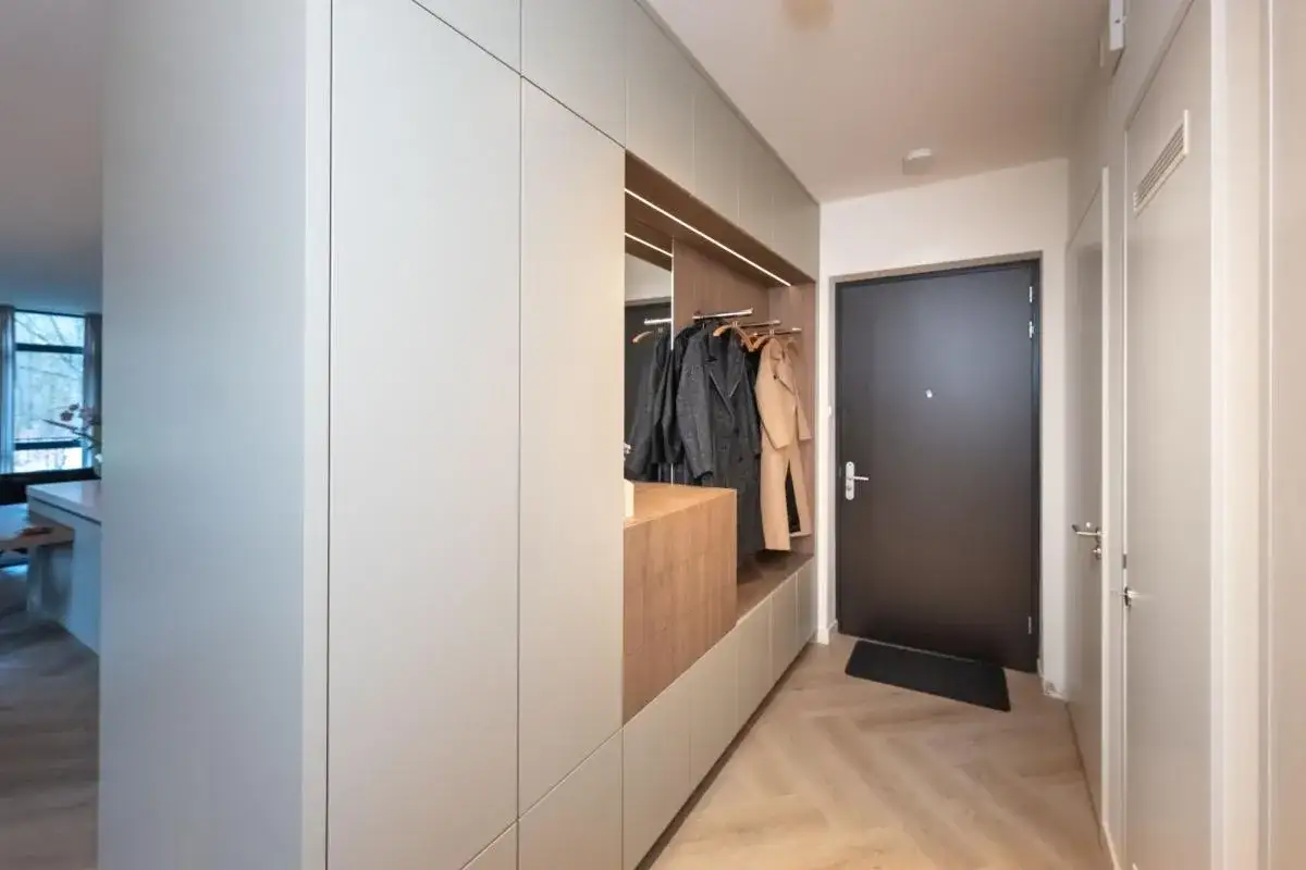 Moderne gang renoveren met strakke kastenwand, open kapstok en houten accenten. Een stijlvolle entree!