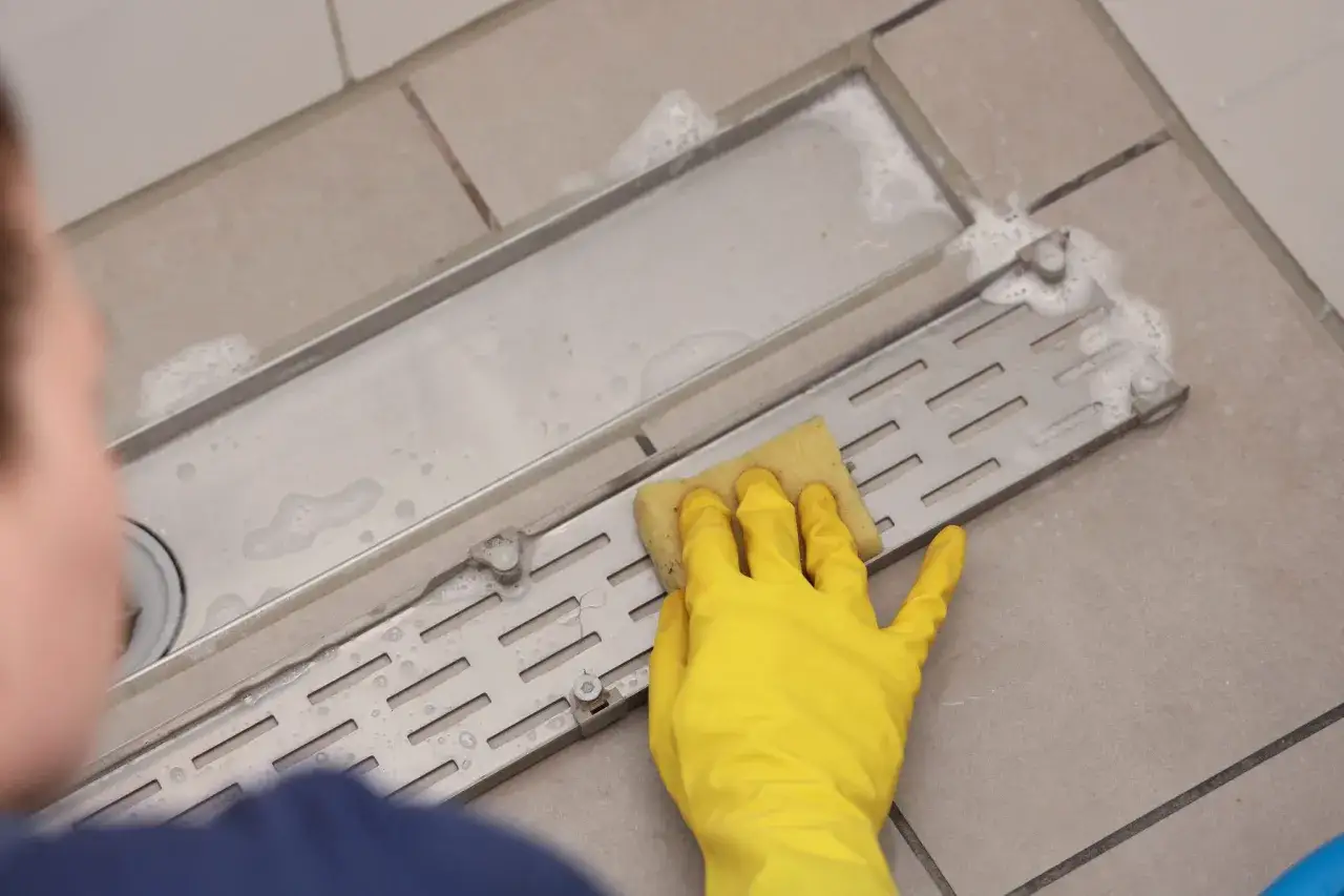 Gele handschoen met spons maakt doucheputje schoon, dat verstopt zit door haren.